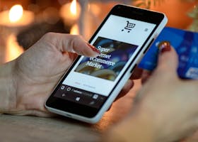 Woman using smartphone for online shopping with credit card in hand, festive background lighting.